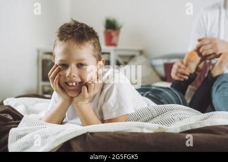 Vater spielt mit seinem Sohn 7-10 auf dem Bett. Papa kitzelt die Füße der Kinder. Familie, die Spaß hat Stockfoto