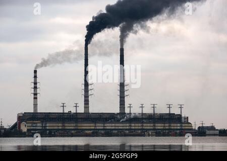 Kohlekraftwerk hohe Rohre mit schwarzem Rauch, der nach oben die verschmutzende Atmosphäre mit den Reflexionen von ihm im Seewasser bewegt. Stockfoto
