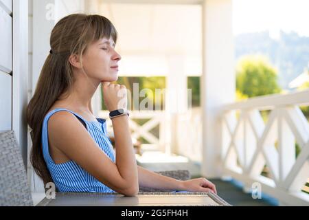 Seitenansicht der schönen Brünette Frau in blauem Kleid sitzt auf gestricktem Stuhl. Konzept der Entspannung an der frischen Luft auf dem Balkon. Stockfoto