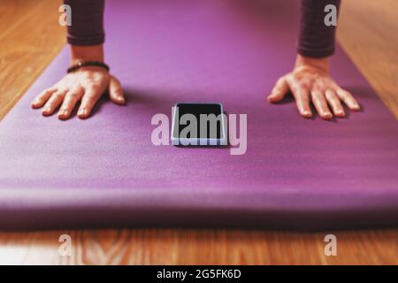 Ein Mädchen macht Yoga mit einem Smartphone online über das Internet auf einem Fliederteppich im Wohnzimmer. Stockfoto