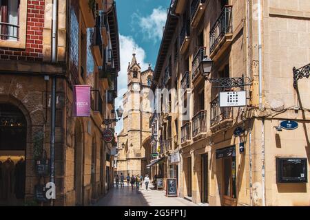 Enge Straße und Kirche mit Uhrenturm in Donostia San Sebastian, Gipuzkoa, Baskenland, Spanien, Europa Stockfoto