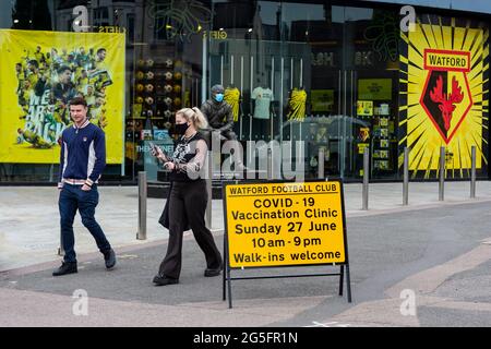 Watford, Großbritannien. 27. Juni 2021. Im Rahmen der „Grab a Jab“-Kampagne passieren Menschen ein Schild vor einer Pop-up-Massenimpfungsklinik im Vicarage Road Stadium des Watford FC. Der NHS fördert dieses Wochenende auch eine Reihe von Walk-in-Kliniken in der Hauptstadt, um zu versuchen, die Zahl der über 18-er-Patienten, die einen Jab erhalten, zu erhöhen, da die Fälle der Delta-Variante laut Berichten auf dem Vormarsch sind. Kredit: Stephen Chung / Alamy Live Nachrichten Stockfoto