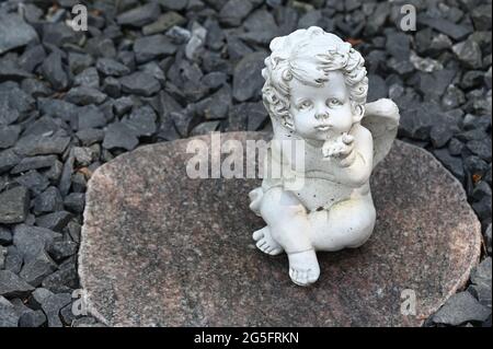 Kitschige Figur eines kleinen Engels auf einem kiesbedeckten Grab Stockfoto