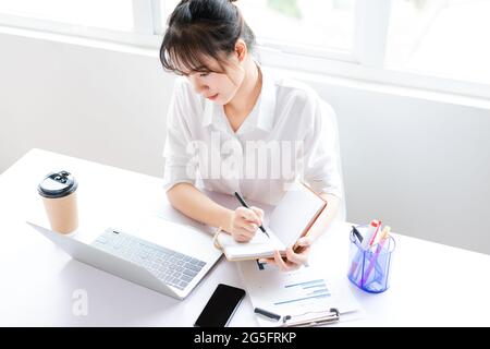 Porträt einer jungen Geschäftsfrau, die in einem Notizbuch sitzt und Pläne macht Stockfoto