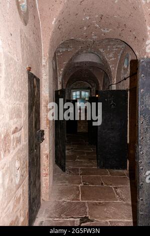 Ein Korridor mit Bögen in der Decke und Steinplatten auf dem Boden beherbergt Gefängniszellen auf beiden Seiten, während sie einen Zellblock im alten Gefängnis von Jedburgh durchqueren Stockfoto