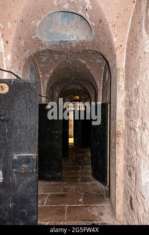 Ein Korridor mit Bögen in der Decke und Steinplatten auf dem Boden beherbergt Gefängniszellen auf beiden Seiten, während sie einen Zellblock im alten Gefängnis von Jedburgh durchqueren Stockfoto