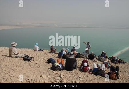 Wanderer, ältere Erwachsene, sitzen auf der Höhe der Judäischen Wüste und hören ihrem Führer zu und sehen die Verdunstungsbecken des Toten Meeres unter und die MTS. Von Moab Stockfoto