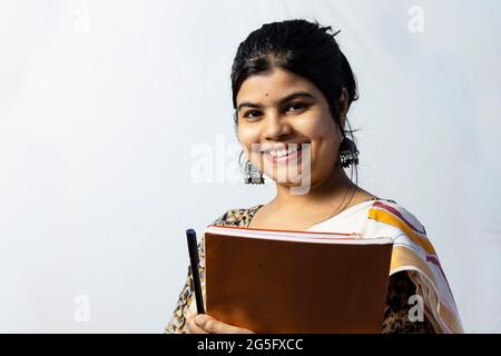 Isoliert auf weißem Hintergrund lächelt eine indische Frau in Saree-Lehrerin mit Büchern in der Hand auf weißem Hintergrund zur Kamera Stockfoto