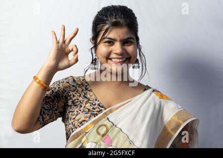 Isoliert auf weißem Hintergrund zeigt ein indisches Weibchen in Saree eine gute Geste mit lächelndem Gesicht auf weißem Hintergrund Stockfoto