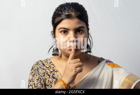 Isoliert auf weißem Hintergrund zeigt ein indisches Weibchen in Saree eine Geste der Stille auf weißem Hintergrund Stockfoto