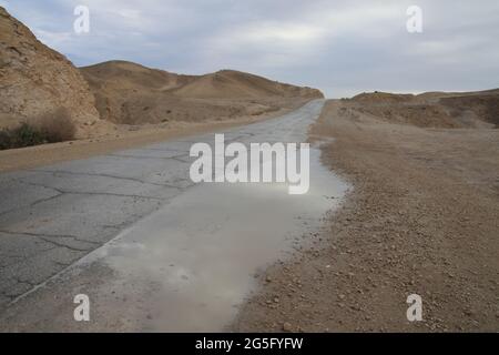 Nasse Landstraße, eine Pfütze mit Spiegelung und Wolken am Himmel, die judäische Wüste nach Regen, ein seltenes Ereignis. Stockfoto