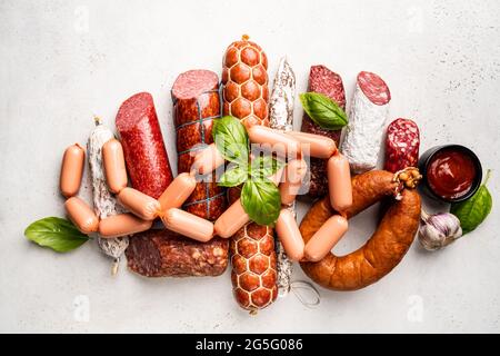 Set aus verschiedenen Wurstsorten, Salami und geräuchertem Fleisch mit Basilikum und Gewürzen auf weißem Hintergrund. Draufsicht. Stockfoto