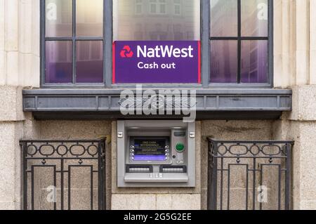 Ein NatWest-Geldautomat in einer Steinmauer einer Bank unter einem Fenster mit dem violetten Zeichen von NatWest. London - 27. Juni 2021 Stockfoto