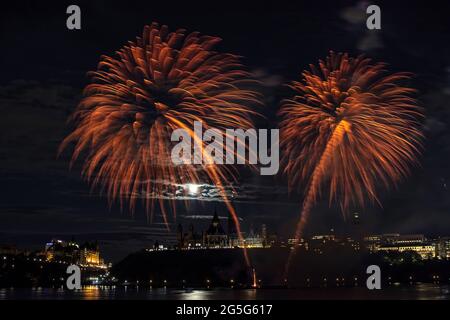 Orangefarbenes Feuerwerk, das durch einen Nachthimmel über den Parlamentsgebäuden hindurchzieht und bei Vollmond die Wolken erleuchtet. Stockfoto