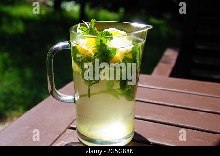Ein kaltes Zitronengetränk in einem Glaskrug. Schöne, frisch zubereitete Limonade. Bio-Minzgetränk mit Zitrusscheiben. Stockfoto