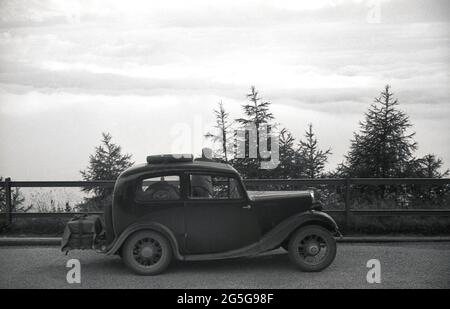 1934, historisch, Touring Bohemia, der westliche Teil der Tschechoslowakei vor WW2. Ein junger Mann, der neben seinem Auto steht, ein britischer Morris Eight, der über die umliegende Landschaft blickt. Dieses Gebiet der Tschechoslowakei war bekannt und wurde zu dieser Zeit als Sudetenland bezeichnet, der historische Name für das sudetendeutsche Volk, das in den westtschechischen Ländern Böhmens und anderen Grenzgebieten lebt. Stockfoto