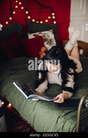 Interessierte Frau, die ein Weihnachtsbuch liest, auf einem Bett liegend Stockfoto