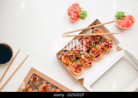 Flaches Set mit Ingwer und Wasabi - gebackenes Sushi-Set mit Lachs in Papierverpackung auf weißem Hintergrund - helles, köstliches Set von Sushi-Rollen Stockfoto