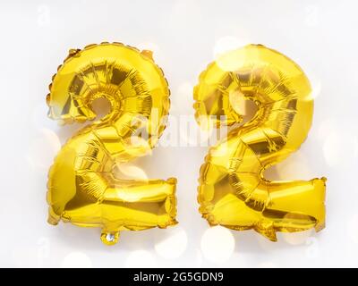 22 goldene Folienballon-Nummern Party-Dekor auf weißem Hintergrund, Geburtstagskonzept mit festlichen Lichtern Stockfoto