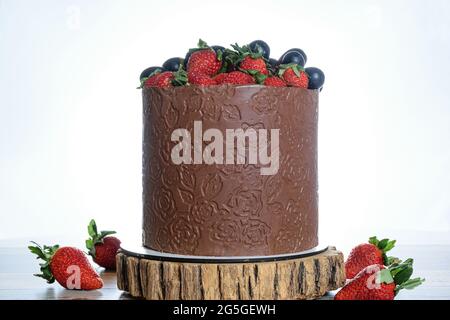 Kuchen in Schokoladenform, verziert mit Trauben und Erdbeeren. Auf einem Holzbalken, Foto mit hohem Schlüssel. Stockfoto