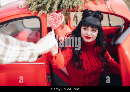 Schöne dunkelhaarige Dame in rotem Pullover, die aus dem Auto aussteigen Stockfoto