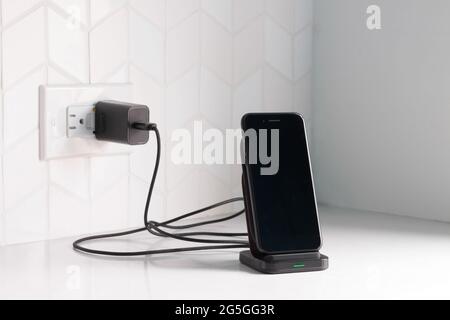 Ein schwarzes Smartphone, das an eine kabellose Ladestation angeschlossen ist und an eine weiße Küchentischplatte oder Bank mit Kopierplatz angeschlossen ist Stockfoto