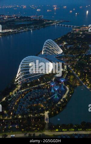 Blick auf die Gärten von Singapur an der Bucht, wenn die Sonne untergeht und die Lichter aufgehen, mit vielen Schiffen in der geschäftigen Straße von Singapur dahinter Stockfoto