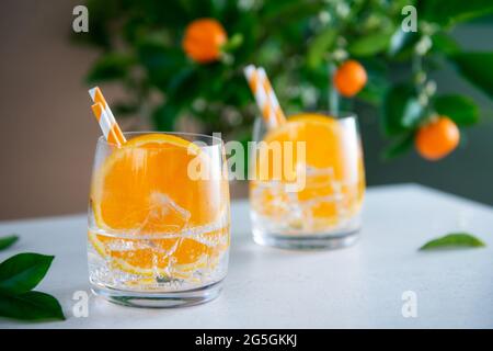 Zwei erfrischende Fruchtcocktails mit Orange, Minze und Eis auf einem weißen Tisch mit Zitrusbaum-Hintergrund. Getränke an der Sommerbar. Selektiver Fiokus, Kopieren Stockfoto