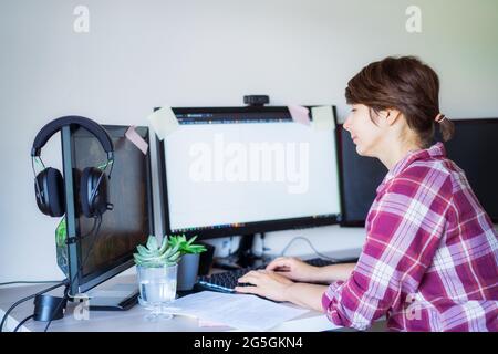 Seitenansicht Frau, die am pc mit wenigen Monitoren im heimischen Arbeitsbereich arbeitet. Remote-Work-Konzept. Freiberufler-Arbeitsbereich. Selektiver Fokus. Speicherplatz kopieren. Stockfoto