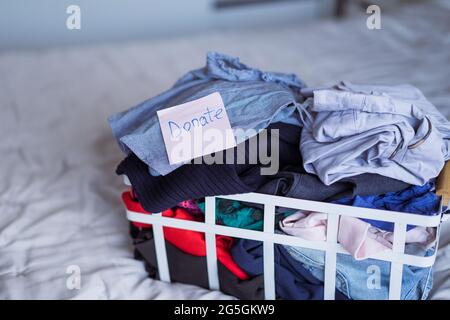 Ein Korb mit ausgewählten Kleidungsstücken für die Spende an einen Charity-Shop, der auf dem Bett steht. Entkleiden, Sortieren Und Aufräumen. Wiederverwenden, aus zweiter Hand Stockfoto