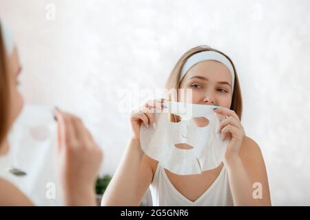 Frau Tragen Sie das Maskenblatt auf das Gesicht auf. Gesichtsbehandlung. Teenager-Mädchen tun Schönheit Gesichtsbehandlung Therapie. Home Beauty Spa-Behandlungen. Tägliche Hygiene und Stockfoto