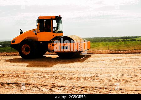 Gelbe schwere Vibrationswalze auf Asphalt funktioniert. Straßenreparatur. Autobahnreparatur an einem sonnigen Sommertag. Schwere Maschinen, Gabelstapler und Lastwagen. Stockfoto