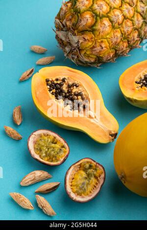 Reif geschnittene Papaya, Ananas, Melone, Passionsfrucht, Mandeln auf blauem pastellfarbenem Hintergrund. Seitenansicht, Nahaufnahme. Tropisches, gesundes Essen, Urlaub, Urlaub c Stockfoto