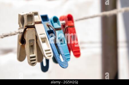 Plastikkleidernadeln hängen in einer Reihe am Seil. Seil im Freien, auf einem verschwommenen Hintergrund in einem sonnigen Garten. Wäscheleine auf der Straße. Wäscheklammern Stockfoto