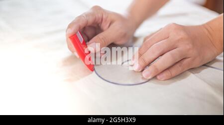 Nahaufnahme der Schneidertisch mit weiblichen Händen zeichnen Stoff mit Kurve Lineal für die Herstellung eines Musters für Kleidung in Werkstatt-Studio. Stockfoto
