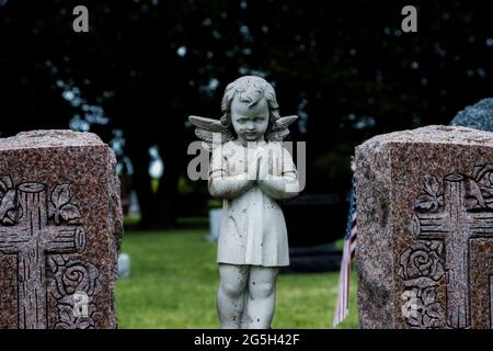 Alte Engelsstatue auf einem Friedhof - kindliche Figur mit gebetteten Händen Stockfoto