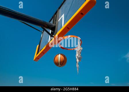 Basketballball fällt durch altes Netz. Auf Spielplatz Blauer Himmel auf Hintergrund Stockfoto