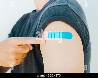 Impfungen, Pflaster auf geimpften Menschen Konzept. Mann Hand zeigt auf blauen Klebstoff Verband auf eigene Schulter, die graue Hemd nach va trägt Stockfoto