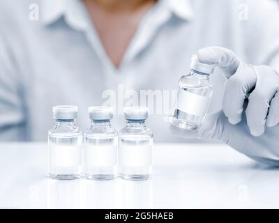 Medizinische Impfstofffläschchen mit weißem Rohling in der Hand des Wissenschaftlers mit weißen Gummihandschuhen. Nahaufnahme von handhaltenden Impfstoffglasflaschen auf Weiß Stockfoto