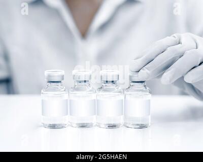 Medizinische Impfstofffläschchen mit weißem Rohling in der Hand des Wissenschaftlers mit weißen Gummihandschuhen. Nahaufnahme von handhaltenden Impfstoffglasflaschen auf Weiß Stockfoto