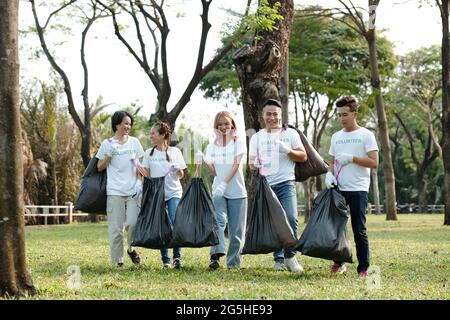 Lächelnde Studenten arbeiten freiwillig im Stadtpark oder auf dem Campus und sammeln Müll in großen Mülltüten Stockfoto