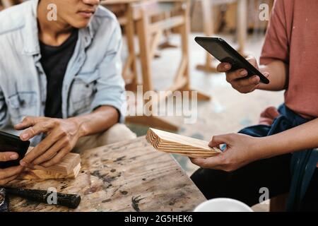 Hände einer jungen Schreinerin, die Fotos von Holzproben fotografiert und in den sozialen Medien hochgeladen hat, um mehr Aufträge zu erhalten Stockfoto
