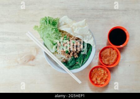 Selektiver Fokus einer Schüssel indonesischer Hühnernudeln, serviert mit Salat, Lauch und Pangsit-Belägen Stockfoto