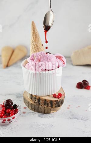 Johannisbeereis mit Waffelkegel und Sirup aus Löffel, auf weißem Granit Stockfoto