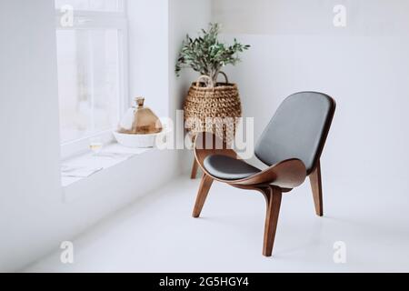 Moderner Sessel aus schwarzem Leder und Holz in einem weißen Loft-Interieur. Designer-Stuhl. Weicher, selektiver Fokus. Stockfoto