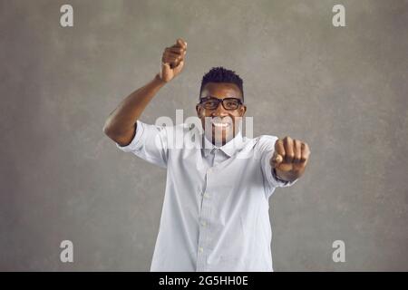 Studioaufnahme eines glücklichen jungen Afro-Amerikaners, der im gangnam-Stil tanzt und lächelt Stockfoto