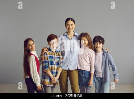 Fröhlich lächelnde Lehrerin posiert mit ihren Schülern auf grauem Hintergrund im Studio Stockfoto