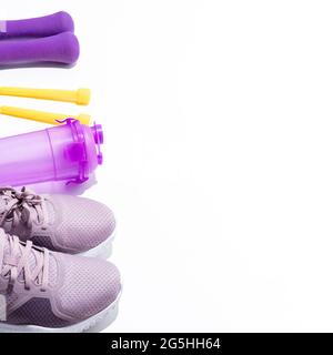 Lila Sneaker, Hanteln, Wasserflasche, gelbes Springseil auf weißem Hintergrund mit Platz für Text. Selektiver Fokus. Stockfoto
