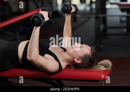 Selbstbewusste und große Frau, die im Fitnessstudio mit Kurzhanteln arbeitet Stockfoto