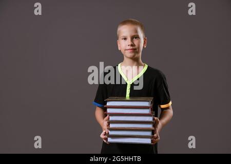 Schuljunge in schwarzem T-Shirt mit einem Stapel Bücher auf grauem Hintergrund Stockfoto